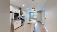 Located at 50 College Ave SE in Grand Rapids, Michigan, this well-appointed one-bedroom, one-bathroom unit offers a thoughtfully designed open-concept layout on a single floor. The combined kitchen, dining, and living area serves as the heart of the space, featuring light hardwood-style flooring and a neutral gray color palette that creates a clean, modern atmosphere. The kitchen is a standout feature, equipped with stainless steel appliances including a refrigerator, electric range, and microwave, all complemented by white shaker-style cabinetry, a gray tile backsplash, a stainless steel range hood, and granite countertops. A central island with an integrated sink and pendant lighting above adds both functionality and style. Natural light flows in through a window at the end of the main living area, enhancing the open feel. The bedroom is carpeted for comfort and includes a window with views of surrounding greenery, providing a quiet retreat. The bathroom is finished with a white vanity featuring a marble-style countertop, a full tub-shower combination, and light wood-tone flooring. An in-unit laundry area adds everyday convenience. This unit combines modern finishes with practical design in a prime Grand Rapids location.