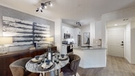 This single-floor residence offers a thoughtfully designed open-concept layout that seamlessly connects the main living areas. The kitchen is outfitted with crisp white shaker cabinetry, granite countertops, a subway tile backsplash, stainless steel appliances including a refrigerator, electric range, microwave, and dishwasher, and a breakfast bar peninsula with a matte black faucet. Wood-look plank flooring runs throughout, adding warmth and continuity across the space. The dining area features a textured accent wall, track lighting, and a built-in nook with granite countertop — ideal for a home office or study space. The living room is bright and open, with crown molding, a ceiling fan, and direct sightlines to the kitchen. The bedroom is a serene retreat highlighted by a bold two-tone navy accent wall, natural window light, and a ceiling fan. The bathroom includes a full tub-shower combination with white tile surround and matte black fixtures. A dedicated in-unit laundry area houses a full-size top-load washer and dryer with overhead shelving, adding everyday convenience to this well-finished, cohesive living space.
