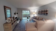 Located at 2101 Park Springs Blvd in Arlington, Texas, this single-story residence offers a well-designed layout with comfortable living spaces and thoughtful finishes throughout. The living room serves as the heart of the home, featuring wood-look flooring, a cozy fireplace, and a large sliding glass door that floods the space with natural light while providing direct access to an outdoor area with pleasant green views. The kitchen is equipped with white cabinetry, speckled quartz-style countertops, black appliances including a refrigerator, range, and microwave, as well as a tile backsplash and track lighting overhead. The home includes multiple bedrooms, each carpeted and fitted with ceiling fans. The primary bedroom offers a sliding closet and a window with sheer curtains, while the additional bedrooms provide generous closet space and natural light. Two bathrooms mirror each other in style, both showcasing wide vanities with speckled countertops, white cabinetry, framed mirrors, and shower/tub combinations. Neutral gray tones are carried throughout the home, creating a cohesive and calming ambiance. The textured ceilings and consistent flooring add to the unified aesthetic of this well-maintained single-floor residence.