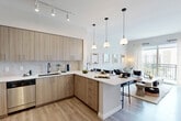 Located at 19277 NW 27th Ave in Miami Gardens, FL, this thoughtfully designed 1-bedroom, 2-bathroom residence offers a modern living experience across a single floor. The open-concept layout seamlessly connects the kitchen, dining area, and living room, creating a bright and cohesive social space. The kitchen is outfitted with light wood cabinetry, white quartz countertops, a full suite of stainless steel appliances, and a peninsula island with bar seating illuminated by elegant pendant lighting. Track lighting and light wood-style flooring carry throughout the main living areas, enhancing the clean, contemporary aesthetic. The living room opens directly onto a private balcony through floor-to-ceiling sliding glass doors, offering views of the surrounding community and abundant natural light. The bedroom is a tranquil retreat featuring a window with outdoor views and generous closet storage. Both bathrooms are finished with neutral tile, wood-toned vanities, and clean white fixtures — one featuring a full soaking tub with shower. Additional conveniences include a dedicated laundry area, entrance foyer, and hallway connecting all spaces efficiently. The overall ambiance is fresh, modern, and welcoming.