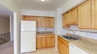 This single-floor residence offers a practical and comfortable layout designed for everyday living. The kitchen is a functional highlight, featuring warm honey-toned wood cabinetry in abundance, providing ample storage above and below the counters. Neutral laminate countertops run throughout, complemented by a stainless steel sink, a gas range with oven, a dishwasher, and a full-size refrigerator. Light ceramic tile flooring and a decorative mosaic tile backsplash accent the space, giving it a clean and cohesive look. The living area is generously proportioned, with soft wall-to-wall carpeting in a neutral beige tone, white walls, and a window that invites natural light and views of surrounding greenery. The open flow of the living space connects seamlessly to additional rooms, enhancing the overall sense of openness. The bedrooms mirror the living area's aesthetic, each featuring plush carpeting and windows that frame outdoor foliage, creating a calm and restful environment. The bathroom is finished with floor-to-ceiling beige tile surrounding a full soaking tub and shower combination, accented by a decorative mosaic tile border. The overall design is understated and neutral, offering a clean, move-in-ready canvas throughout.