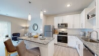 This one-bedroom, one-bathroom residence in Blue Springs, Missouri offers a thoughtfully designed layout with modern finishes throughout. The open-concept kitchen and living area serves as the heart of the home, where crisp white shaker cabinets, granite countertops, a subway tile backsplash, and a full suite of stainless steel appliances — including a refrigerator, range, microwave, and dishwasher — create a polished, functional space. A granite-topped kitchen island with pendant lighting provides additional seating and prep space, while light wood-style flooring runs throughout the main living areas, enhancing the bright and airy atmosphere. The living room is anchored by a large sliding glass door dressed with vertical blinds, allowing generous natural light and outdoor views to fill the space. The bedroom offers a comfortable, carpeted retreat with a ceiling fan, a large window with exterior views, and dedicated closet storage. The bathroom features a white vanity with granite countertops, wood-style flooring, and a shower-tub combination. Neutral warm tones and clean architectural lines are consistent throughout, contributing to a cohesive and inviting overall ambiance.