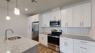 This single-floor residence showcases a thoughtfully designed open-concept layout where the kitchen flows seamlessly into the living area. The kitchen is a standout feature, equipped with white shaker-style cabinetry extending to the ceiling for ample storage, granite countertops, and a full stainless steel appliance suite including a French door refrigerator, electric range, and over-the-range microwave. A classic white subway tile backsplash adds a clean, timeless aesthetic, while a large center island with a light blue base, granite top, and an integrated sink serves as a functional focal point, illuminated by pendant lighting above. Wood-look flooring runs throughout the main living and kitchen areas, complementing the bright, neutral color palette.

The living area is generously sized with a ceiling fan and connects directly to the kitchen, creating an ideal space for entertaining. Bedrooms feature plush carpeting, ceiling fans, and natural light from windows. The primary bedroom connects to a bathroom with a glass-enclosed tub-shower combination, white tile with contrasting black mosaic accents, a granite-topped vanity, and tile flooring. A second bathroom mirrors similar finishes with a white vanity and granite countertop.