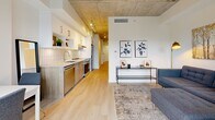 Located at 825 Fort Street in the heart of Victoria, BC, this thoughtfully designed one-bedroom, one-bathroom unit blends urban industrial aesthetics with modern comfort. The space is defined by its signature exposed concrete ceiling, which carries throughout the unit and lends a distinctive loft-inspired character to every room.

The open-concept living and kitchen area forms the heart of the unit. The kitchen features white upper cabinetry, warm wood-toned lower cabinets, a subway tile backsplash, and stainless steel appliances, including a range and dishwasher. Light hardwood flooring runs seamlessly into the living area, where large glass doors open onto a private balcony with glass railings, flooding the space with natural light and offering outdoor access.

The hallway, accented with a sliding barn door and a keypad entry, connects the main living area to the private rooms. The bedroom is a cozy retreat, highlighted by an exposed concrete accent panel, light walls, and warm-toned hardwood floors. The bathroom is clean and modern, featuring floor-to-ceiling white tile and a glass-enclosed shower with gold-toned hardware accents.

This unit's combination of industrial design elements, natural light, and functional layout makes it a refined urban residence in downtown Victoria.
