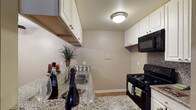 This single-floor residence offers a thoughtfully designed layout centered around a functional and stylish kitchen. The kitchen is a standout feature, showcasing granite countertops that provide ample prep space and a durable, attractive surface. White upper cabinetry lines the walls, offering generous storage while contributing to a bright, clean aesthetic. Black appliances, including a gas range and overhead microwave, provide a bold contrast against the lighter tones of the cabinetry and counters. A stainless steel sink is neatly integrated into the countertop, adding a practical and modern touch. The kitchen is illuminated by a flush-mount ceiling light that evenly brightens the space. Neutral-toned walls and light hardwood flooring create a warm, cohesive atmosphere throughout. The overall design balances practicality with visual appeal, making the kitchen both a highly functional workspace and an inviting area. The single-floor layout ensures easy accessibility and a seamless flow throughout the residence, making it a comfortable and efficient space for everyday living.