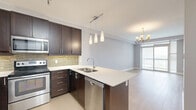 Located at 15 Maple Ave in Barrie, Ontario, this well-designed 2-bedroom, 2-bathroom unit offers a thoughtful layout across a single floor. The open-concept kitchen and living area serves as the heart of the home, featuring rich dark-stained cabinetry, stainless steel appliances including a full-size refrigerator, electric range, and built-in microwave, complemented by a tasteful tile backsplash and light quartz countertops. A large central island with a double undermount sink and pendant lighting above provides additional workspace and a natural gathering point. Light hardwood flooring flows throughout the main living areas, adding warmth to the neutral grey palette. The spacious primary bedroom offers a generous footprint with a sliding glass door leading to an outdoor balcony, allowing for ample natural light and elevated views of the surrounding Barrie cityscape. The second bedroom is carpeted and bright, with large windows framing city views. Both bathrooms are finished with dark wood vanities, quartz counters, and large-format tile flooring. A dedicated in-unit laundry area houses a stacked washer and dryer. The unit also includes a closet for additional storage, completing this practical and modern urban residence.