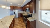 This well-appointed 2-bedroom, 2-bathroom residence offers a thoughtfully designed single-level layout. The kitchen serves as a central highlight, showcasing rich dark cabinetry, granite countertops, a decorative tile backsplash, and a full suite of stainless steel appliances including a refrigerator with ice maker, electric range, and built-in microwave. A kitchen island with matching granite provides additional prep space and is illuminated by modern pendant lighting. Hardwood-style flooring flows throughout the main living areas, complemented by neutral taupe walls that create a warm, cohesive atmosphere. The living area features sliding glass doors that open to a balcony, allowing natural light to fill the space. Both bedrooms are generously sized with plush carpeting and windows fitted with roller shades for privacy. The primary bathroom is elongated and features a dual-sink vanity with white countertops, dark wood cabinetry, and a tiled walk-in glass shower. The second bathroom is equally well-finished, offering a full soaking tub and shower combination, a single-sink vanity, and consistent hardwood-style flooring that ties the design together throughout the unit.
