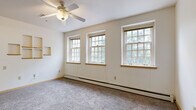 This single-floor, 2-bedroom, 1-bathroom unit offers a straightforward and functional layout, thoughtfully arranged to maximize the use of its compact footprint. A hallway connects the main areas of the unit, providing a clear sense of flow from room to room.

The primary bedroom is the standout space, featuring plush wall-to-wall carpeting, a ceiling fan with integrated lighting, and multiple multi-pane windows that bathe the room in natural light while offering leafy outdoor views. Built-in wall shelving adds a practical and distinctive design touch. Baseboard heating runs along the exterior walls, ensuring year-round comfort. The second bedroom mirrors a similar aesthetic with carpeted floors, multi-pane windows, and baseboard heating.

The kitchen is efficiently designed with warm honey-toned wood cabinetry offering ample upper and lower storage, laminate countertops, and wood-look vinyl flooring. A freestanding electric range with overhead ventilation anchors the cooking area.

The bathroom is clean and well-appointed, featuring a wood-toned vanity with a white countertop, an integrated sink, under-counter storage drawers, and a large mirror above. Neutral wall tones and tile flooring complete the space.

Throughout the unit, neutral wall colors, consistent carpeting, and plentiful natural light from multi-pane windows create a bright, cohesive, and livable environment.