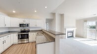 This single-floor residence showcases a clean, modern design throughout its well-organized layout. The open-concept kitchen flows directly into the living area, creating a connected and functional space. The kitchen is equipped with stainless steel appliances, including a refrigerator, range, and microwave, all complemented by crisp white shaker-style cabinetry and granite countertops. A peninsula with matching granite extends into the living area, offering additional workspace and a natural division between the two spaces. The living room features vaulted ceilings that add a sense of openness, along with a ceiling fan and a tiled fireplace that serves as a focal point.

The bedrooms are carpeted and each includes a ceiling fan and windows that allow natural light to filter in. One bedroom provides direct access to a dedicated laundry closet housing a stacked washer and dryer unit. The unit includes two bathrooms: one with a soaking tub and granite-topped vanity, and another with a walk-in shower, matching vanity, and white cabinetry for storage. Both bathrooms feature wood-look luxury vinyl flooring, consistent with the kitchen and bathroom areas, while soft carpet covers the living and bedroom spaces throughout.