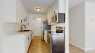 This single-floor residence offers a thoughtfully arranged layout across several distinct living areas. The galley-style kitchen serves as a functional centerpiece, outfitted with crisp white cabinetry accented by matte black hardware and marble-look countertops that lend a clean, modern aesthetic. A deep undermount sink with a brushed dark faucet sits alongside a full suite of stainless steel appliances, including a refrigerator, electric range, over-the-range microwave, and dishwasher. A textured ceiling and flush-mount light fixture complete the kitchen's practical design.

The living areas feature light hardwood-style flooring that reflects natural sunlight generously admitted through large windows dressed with vertical blinds. Baseboard heating lines the perimeter walls, and ceiling fans are present in multiple rooms. The bedrooms are finished with plush carpeting, offering a softer, quieter atmosphere, and each benefits from natural light and ceiling fan fixtures.

The bathroom includes a full tub-shower combination with bright white surround, a white vanity with matching cabinetry, and warm hardwood-style flooring. Throughout the unit, a neutral color palette of whites and soft beiges creates a clean, cohesive, and move-in-ready environment.