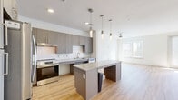 This well-appointed 1-bedroom, 1-bathroom unit offers a thoughtfully designed open-concept layout that maximizes every square foot of living space. Light hardwood flooring flows throughout the main living areas, lending warmth and continuity to the interior. The kitchen is a standout feature, showcasing grey shaker-style cabinetry, granite countertops, a white subway tile backsplash, and a full suite of stainless steel appliances including a refrigerator, range, dishwasher, and built-in microwave. A central kitchen island with pendant lighting above provides additional prep and seating space. The living area is bright and airy, benefiting from large windows and a ceiling fan that together promote natural light and airflow. French doors in the living space offer an additional source of natural light and outdoor access. The bedroom features plush carpeting, sun-filled windows, and a walk-in closet equipped with built-in shelving and hanging rods for organized storage. The full bathroom is finished with granite countertops, grey cabinetry, a combined tub and shower, and hardwood flooring, with accessibility-friendly features integrated into the design. The overall aesthetic is clean, contemporary, and move-in ready.
