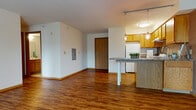 Located at 2 W Gorham St in the heart of Madison, Wisconsin, this single-floor residential unit offers a practical and comfortable layout with consistent warm-toned hardwood-style flooring throughout. The open living area is generously sized, bathed in natural light from large windows, and features baseboard heating and a wall-mounted AC unit, ensuring year-round comfort. Clean white walls and neutral finishes create a bright, versatile atmosphere throughout.

The kitchen is well-equipped with warm oak cabinetry, granite-style countertops, a white appliance suite including a range and refrigerator, and an under-cabinet range hood. A peninsula with a stone-topped breakfast bar extends into the living space, illuminated by stylish pendant lighting on a track rail system — making it ideal for casual dining or entertaining.

The bedroom is a quiet, well-proportioned room with the same hardwood-style flooring, natural light from a window, and a built-in closet with wood-panel doors. The bathroom features tile flooring, an oak vanity with storage, and a clean, functional layout. Throughout the unit, wood-panel interior doors and wood trim add a cohesive, warm character to the space.