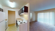 Located at 2420 Tate Springs Rd in Lynchburg, Virginia, this single-floor unit offers a practical and straightforward layout across several well-defined spaces. The galley-style kitchen is efficiently arranged with dark wood cabinetry overhead, a white electric coil-burner range, a full-size refrigerator, and light-toned countertops. Tile flooring runs through the kitchen, which opens toward the living area. The living space features carpet flooring and a sliding glass door fitted with vertical blinds, allowing natural light to filter in. A separate dining area is distinguished by two-tone walls with a chair rail, complemented by a modest chandelier overhead and tile flooring. The bedrooms are carpeted and receive natural light through blinds-covered windows. One bedroom features a spacious walk-in closet with dual shelving sections, offering generous storage capacity. A second bedroom also includes closet access. Two bathrooms are present, each featuring a tub-shower combination with light blue tile surrounds, a vanity with a mirrored medicine cabinet, and standard fixtures. The overall layout is functional and straightforward, suited for everyday living.