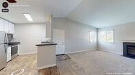 This two-bedroom, one-bathroom apartment at Shapiro Apartments in Rocklin, California offers a well-designed single-floor layout with a bright, neutral palette throughout. The open living area features vaulted ceilings that enhance the sense of space, plush carpet flooring, and a ceiling fan. A kitchen peninsula with a dark countertop creates a natural transition between the kitchen and living space, where wood-look vinyl flooring runs underfoot. The kitchen is equipped with stainless steel appliances — including a range, over-the-range microwave, and dishwasher — complemented by white shaker-style cabinetry and gray countertops. A window allows natural light to fill the space. The living room opens to a private balcony through sliding glass doors with vertical blinds, offering pleasant outdoor views of surrounding greenery. Both bedrooms are carpeted and feature neutral gray walls, with windows that bring in natural light. The full bathroom includes a tub/shower combination and wood-look flooring. A dedicated in-unit laundry area accommodates a full-size washer and dryer, topped with additional storage cabinetry. This apartment provides a comfortable and functional living environment in a convenient Rocklin location.