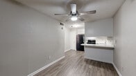 This single-floor residence offers a practical and well-appointed layout designed for comfortable everyday living. The open-concept living area flows seamlessly into the kitchen, creating a connected and functional space. A ceiling fan with an integrated light fixture is prominently positioned overhead, providing both airflow and ambient lighting. The floors throughout are finished in wood-look planks in a neutral gray-brown tone, lending warmth and visual continuity across the space.

The kitchen is equipped with white cabinetry offering generous storage, black appliances including a full-size refrigerator and electric range, and a light-toned countertop that extends into a peninsula with a curved edge — ideal as a breakfast bar or additional prep surface. A single-basin sink is positioned beneath upper cabinets, with a simple yet functional layout.

The bedroom features its own ceiling fan, a large window fitted with horizontal blinds that allows for natural light, and the same wood-look flooring carried throughout. The textured walls add subtle visual character to the room.

The bathroom includes a white vanity with a light stone-style countertop, a framed mirror, white cabinetry for additional storage, and a dedicated walk-in shower stall with white tile surround. The overall aesthetic of the residence is clean, neutral, and move-in ready.