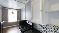This well-appointed 1-bedroom, 1-bathroom residence offers a comfortable and thoughtfully designed single-floor layout. The kitchen stands out with its striking contrast of white shaker-style cabinetry paired with a bold black gas range and dark countertops. A patterned black-and-white geometric tile backsplash adds a decorative focal point, giving the kitchen a distinct, stylish character. The walls are finished in a cool gray tone that complements the overall aesthetic, while crown molding details add a touch of classic refinement. Natural light filters in through the windows, brightening the space and enhancing its open feel. The flooring throughout features warm-toned hardwood, providing a cohesive and inviting atmosphere. The single-level floor plan ensures easy navigation between living areas, making everyday use practical and efficient. Overall, the space balances modern design elements with functional living, making it a comfortable home that combines style and utility in a compact yet well-utilized footprint.