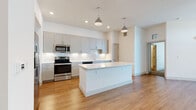 This single-floor residence is designed with a clean, contemporary aesthetic throughout. The kitchen serves as a central highlight, featuring gray shaker-style cabinetry, white quartz countertops, and a classic subway tile backsplash. A generous island with a crisp white finish anchors the space, while industrial-style pendant lights hang overhead. Stainless steel appliances, including a French door refrigerator, range, and built-in microwave, provide a polished, functional finish. Warm-toned hardwood-style flooring flows throughout the kitchen and living areas, complementing the bright white walls and recessed lighting.

The bedrooms are carpeted and well-lit by natural light through large windows with blinds, each equipped with a ceiling fan. Multiple walk-in closets offer dual hanging rods and shelving on three sides, providing substantial storage.

The bathrooms are finished with gray shaker vanities, white quartz countertops, and chrome hardware. The primary bath includes a glass-enclosed walk-in shower with subway tile surround, while a secondary bath features a vanity with ample cabinetry and a lighted mirror. The overall ambiance is bright, neutral, and move-in ready.
