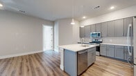 This well-appointed single-story residence in Austin, TX offers three bedrooms, two bathrooms, and a thoughtfully designed layout that maximizes both comfort and functionality. The open-concept kitchen serves as the heart of the home, showcasing sleek gray shaker cabinetry, a white quartz countertop island with a built-in sink, and a full suite of stainless steel appliances including a gas range, over-the-range microwave, dishwasher, and French door refrigerator. A classic subway tile backsplash and modern pendant lighting complete the space. Light wood-style flooring flows throughout the main living areas, creating a warm and cohesive aesthetic. The bedrooms are carpeted and filled with natural light from well-positioned windows fitted with blinds, offering views of the surrounding neighborhood. The primary bedroom includes a walk-in closet with built-in shelving and hanging rods. The bathrooms feature large-format tile flooring, marble-look wall tile, gray vanity cabinetry with white countertops, and framed mirrors. With four total closets and a connecting hallway, the layout provides ample storage. The neutral color palette and modern finishes throughout create a clean, contemporary ambiance suited for everyday living.