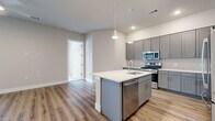 This well-appointed single-story residence in Austin, TX offers three bedrooms, two bathrooms, and a thoughtfully designed layout that maximizes both comfort and functionality. The open-concept kitchen serves as the heart of the home, showcasing sleek gray shaker cabinetry, a white quartz countertop island with a built-in sink, and a full suite of stainless steel appliances including a gas range, over-the-range microwave, dishwasher, and French door refrigerator. A classic subway tile backsplash and modern pendant lighting complete the space. Light wood-style flooring flows throughout the main living areas, creating a warm and cohesive aesthetic. The bedrooms are carpeted and filled with natural light from well-positioned windows fitted with blinds, offering views of the surrounding neighborhood. The primary bedroom includes a walk-in closet with built-in shelving and hanging rods. The bathrooms feature large-format tile flooring, marble-look wall tile, gray vanity cabinetry with white countertops, and framed mirrors. With four total closets and a connecting hallway, the layout provides ample storage. The neutral color palette and modern finishes throughout create a clean, contemporary ambiance suited for everyday living.