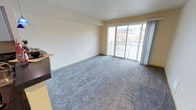 Located in the vibrant Fremont neighborhood of Seattle, Unit 516 at 620 N 34th Street is a single-floor residence that combines comfort with natural light. The main living area is generously proportioned, featuring soft wall-to-wall carpeting in a neutral blue-grey tone that adds warmth underfoot. Smooth, light-colored walls and a clean white ceiling create a bright, open atmosphere throughout the space. A standout feature of the living area is the large sliding glass door that opens directly onto a private balcony, allowing abundant natural light to pour into the room while offering elevated views of the surrounding Seattle landscape. The balcony, framed by a white railing, provides an inviting outdoor extension of the living space. Sheer curtain panels flank the glass door, offering flexible light control while maintaining the airy feel of the room. A partial view of what appears to be a kitchen counter or bar surface is visible at the edge of the living area, suggesting a connected, open layout. Overall, the unit presents a clean, move-in ready interior with a welcoming ambiance, well-suited for those seeking a comfortable residence in one of Seattle's most sought-after neighborhoods.