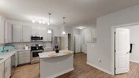 This single-floor residence offers a thoughtfully designed layout that balances style and functionality throughout. The kitchen serves as the heart of the home, showcasing gray shaker-style cabinetry, granite-look countertops, and a full suite of stainless steel appliances including a refrigerator, range, microwave, and dishwasher. A central island provides additional prep space and casual seating, while pendant lighting and a track light fixture add a contemporary touch overhead. Wood-look flooring runs through the kitchen and living areas, lending warmth and continuity to the open layout. A dedicated pantry offers generous storage just steps from the cooking area. The bedrooms feature plush carpeting and ceiling fans with light fixtures, creating a comfortable retreat. Multiple windows dressed with blinds allow natural light to filter in while maintaining privacy. Walk-in closet space with built-in shelving provides practical storage in the sleeping quarters. The bathroom is finished with granite-look countertops, wood-look flooring, and clean, neutral tones throughout. An in-unit laundry area adds everyday convenience. The overall aesthetic is clean and modern, with a neutral color palette of whites and soft grays that creates a bright, cohesive ambiance across the entire space.