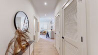 This single-floor residence showcases a cohesive modern design characterized by light oak hardwood flooring, crisp white walls, and black hardware accents that carry consistently throughout the space. The welcoming entryway corridor features louvered double doors, a decorative console, and a round mirror, leading naturally toward the heart of the home.

The open-concept living area is anchored by a linear gas fireplace set within a white tile surround, a wall-mounted television, and generous seating space. Large windows and sliding glass doors invite abundant natural light and provide access to an outdoor area. The space flows seamlessly into a dining area and kitchen, where an island with bar seating sits beneath a sculptural branching chandelier.

The bedrooms maintain the home's serene palette, with tall ceilings, natural light from oversized windows with outdoor views, and warm wood flooring. One bedroom benefits from a wraparound window arrangement that floods the room with sunlight.

Two well-appointed bathrooms are finished in neutral stone-look tile. One features a walk-in glass shower with matte black fixtures and a floating vanity, while the second offers a vessel sink, warm-toned wood cabinetry, and refined gold accents. The overall ambiance throughout is calm, contemporary, and thoughtfully curated.