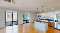 This well-appointed single-floor residence offers a clean, contemporary design throughout. The open-concept living and kitchen area serves as the heart of the space, flooded with natural light from large floor-to-ceiling windows and sliding glass doors that overlook surrounding brick architecture. Warm hardwood flooring extends seamlessly across the main living areas, enhancing the bright and airy ambiance.

The kitchen is thoughtfully designed with white cabinetry, dark granite countertops, a central island with pendant lighting, track lighting overhead, and a full suite of stainless steel appliances including a range, over-the-range microwave, dishwasher, and a side-by-side refrigerator with ice and water dispenser. A dedicated hallway leads to the private areas of the residence, including a bedroom with a ceiling fan and a spacious walk-in closet outfitted with wire shelving systems for ample storage.

The bathroom features large-format white tile flooring, a sleek dark vanity with a clean white countertop, and a glass-enclosed shower with classic white subway tile. A notable convenience is the in-unit laundry area, which houses a side-by-side washer and dryer tucked neatly behind a sliding panel door. A ceiling-mounted HVAC unit in the living area ensures efficient climate control throughout.