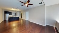 This 1-bedroom, 1-bathroom residence offers a thoughtfully designed single-floor layout that balances modern style with everyday functionality. Rich, dark hardwood flooring flows throughout the living areas and bedroom, lending warmth and continuity to the space.

The open-concept living and dining area is generously proportioned, featuring neutral gray walls, ceiling fans, and track lighting that provide both comfort and versatility. The space connects seamlessly to the kitchen, which serves as a striking focal point with bold dark cabinetry, a large granite-topped island with a built-in sink, stainless steel appliances including a refrigerator, range, and microwave, and a classic white subway tile backsplash. A linear pendant light above the island adds a contemporary touch.

The bedroom is well-sized and bright, benefiting from a large window that welcomes natural light. A ceiling fan overhead and direct access to the bathroom enhance its practicality. The bathroom is clean and modern, featuring light tile flooring, a full tub-shower combination with white subway tile surround, and a dark vanity. An adjacent walk-in closet provides ample storage. Throughout the residence, the design emphasizes clean lines, neutral tones, and quality finishes.