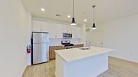 This contemporary 680 square foot apartment in Cherry Hill, NJ, offers a well-designed living space with modern amenities. The single-floor layout comprises one bedroom, one bathroom, and an open-concept kitchen and living area. The primary bedroom, spanning 200 square feet, provides ample space for relaxation and storage.

The apartment features light-toned wood-look flooring throughout, creating a seamless flow between rooms. Large windows in the living area and bedroom allow for abundant natural light, enhancing the sense of spaciousness. The kitchen boasts sleek white cabinetry, stainless steel appliances, and a central island with a white countertop, perfect for meal preparation or casual dining.

The bathroom continues the modern aesthetic with a wood-grain vanity, white countertop, and a large mirror. A combination tub and shower with white tiling completes the space. The bedroom includes a walk-in closet for added storage convenience.

Recessed lighting and pendant fixtures in the kitchen provide layered illumination options. The neutral color palette of whites and light woods creates a fresh, clean ambiance that can easily accommodate various decor styles. This apartment offers an ideal blend of functionality and contemporary design for comfortable city living.