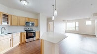 Located at 7400 Flying Cloud Dr in Eden Prairie, MN, this two-bedroom, one-bathroom residence offers a well-designed single-level layout with a thoughtful mix of materials and finishes throughout. The open-concept kitchen and living area serves as the heart of the home, featuring warm honey-toned cabinetry, stainless steel appliances including a range, microwave, dishwasher, and refrigerator, and a central island with a clean white countertop illuminated by pendant lighting. Hardwood-style flooring runs through the main living areas, adding warmth and continuity to the space. The living room benefits from large corner windows that invite abundant natural light and offer elevated views of the surrounding Eden Prairie landscape. The spacious primary bedroom continues the hardwood-style flooring and features generous windows with scenic outdoor views. The second bedroom is finished with plush carpeting, offering a cozy retreat. A walk-in closet with wire shelving provides ample storage. The full bathroom is well-appointed with an L-shaped dual-sink vanity, warm wood cabinetry, white countertops, and a large wall mirror. A connecting hallway ties the layout together efficiently, completing this comfortable and functional residence.