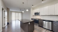 Located on W First St N in Wichita, Kansas, this well-appointed 2-bedroom, 2-bathroom residence offers a thoughtfully designed single-level floor plan with modern finishes throughout. The open-concept kitchen and dining area serves as the heart of the home, showcasing a striking two-tone cabinet scheme — crisp white upper cabinets paired with dark lower cabinets — complemented by granite countertops, a subway tile backsplash, a center island, and a full suite of stainless steel appliances including a refrigerator, range, microwave, and dishwasher. Pendant lighting and recessed track lighting enhance the space's contemporary aesthetic. Wood-look luxury vinyl plank flooring flows through the main living areas, while a ceiling fan and large vertical-blind-covered sliding door bring comfort and natural light to the living room. A central hallway connects both bedrooms, each fitted with plush carpet and ceiling fans. The primary bedroom features generous closet storage. The two bathrooms are well-finished — one with a sleek glass-enclosed walk-in shower, the other with a full soaking tub and a dark-cabinet vanity with granite countertops. A dedicated in-unit laundry area with a full-size washer and dryer completes this practical and stylish home.