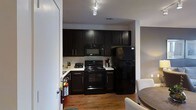 This multi-story residence spans three floors, offering a well-organized and functional layout throughout. The kitchen is a standout feature, designed with a sleek, contemporary aesthetic. Dark espresso-toned cabinetry lines the walls, providing ample storage space, while light-colored countertops create a striking contrast. A full suite of black appliances — including a refrigerator, electric range, and over-the-range microwave — gives the kitchen a cohesive, modern look. Track lighting overhead ensures the space is well-lit, highlighting the warm hardwood flooring that flows through the area and adds a welcoming, natural element to the interior. The kitchen opens toward a dining and living area, suggesting a connected, open-concept flow between common spaces. Neutral wall tones throughout contribute to a clean, versatile backdrop that complements the bold kitchen finishes. The three-floor layout provides distinct zones for living, sleeping, and utility, offering a sense of separation and privacy across levels. Overall, the space presents a modern and functional interior with thoughtful design details and a bold yet balanced color palette.