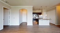 This single-floor residence offers a thoughtfully designed layout with consistent hardwood-style flooring flowing throughout the main living areas and bedrooms. The open living room is generously proportioned, featuring crown molding, a ceiling fan, and a bank of windows fitted with blinds that invite natural light while offering views of the surrounding exterior. An elegant arched entryway connects the living space to the kitchen and entry foyer, adding a refined architectural detail.

The kitchen is a standout feature, showcasing rich dark cabinetry with decorative panel detailing, granite countertops, a subway tile backsplash, and a full suite of stainless steel appliances including a range, microwave, refrigerator with ice maker, and dishwasher. A double-basin sink and pendant lighting over the island enhance both function and style. A set of double doors provides access to a pantry or additional storage.

The bedrooms continue the wood-style flooring and crown molding theme, each equipped with ceiling fans. The primary bedroom includes a walk-in closet with built-in shelving. The bathrooms are finished with dark vanity cabinetry, granite countertops, and large-format tile surrounds in the tub-shower combinations, complemented by chrome fixtures throughout. The overall ambiance is clean, modern, and move-in ready.