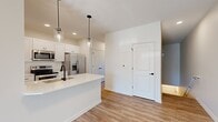 Located at 113 East Genesee Pointe Drive in West Henrietta, NY, this well-appointed 2-bedroom, 3-bathroom home offers a thoughtfully designed single-floor layout. The open-concept kitchen and living area serves as the heart of the home, featuring crisp white shaker cabinetry, quartz countertops, a central island with an undermount sink and matte black faucet, and a full suite of stainless steel appliances including a refrigerator with ice maker, electric range, and microwave. Stylish pendant lights hang above the island, adding a modern touch. Light-toned hardwood-style flooring flows throughout the main living areas, enhancing the bright, airy atmosphere. The living room opens to a private deck through sliding glass doors, bringing in abundant natural light and outdoor views. The primary bedroom is a comfortable retreat, complete with a dedicated en-suite bathroom featuring a white vanity with quartz countertop, a framed mirror with matte black accents, and a walk-in closet with built-in shelving. The second bedroom is carpeted and well-proportioned. All three bathrooms maintain a consistent, clean aesthetic with white cabinetry and modern fixtures. The home's neutral palette and contemporary finishes create a cohesive, move-in-ready environment.