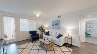 Located at Wagon Wheel Road in Oxnard, California, this single-story unit presents a cohesive coastal aesthetic throughout its well-designed layout. The living area serves as the heart of the home, featuring wood-style flooring, a ceiling fan, and generous natural light streaming through wide windows fitted with horizontal blinds. A sliding glass door provides access to an outdoor area, further enhancing the bright, airy atmosphere. The space comfortably accommodates a seating arrangement centered around a rustic coffee table.

The kitchen is well-appointed with white shaker-style cabinetry, granite countertops, and a full suite of stainless steel appliances, including a gas range, microwave, refrigerator, and dishwasher. Recessed lighting and a window above the sink add to the clean, functional design.

The bedrooms continue the light coastal theme, each featuring plush carpeting, ceiling fans, and ample natural light from well-placed windows. The bathroom includes a tub-shower combination with white subway tile surround, wood-style flooring, a vanity with a light countertop, and a large mirror. The overall ambiance of the unit is calm, clean, and cohesive, reflecting a relaxed Southern California coastal sensibility.