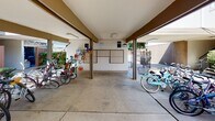 The outside entry and pool area at 801 D St in Davis, California offers a well-organized and functional communal exterior space designed to serve residents with everyday conveniences. The entry area features a covered, open-air structure with a concrete floor that provides shelter for bicycle parking, with multiple bike racks accommodating a generous number of bicycles — reflecting the bike-friendly culture of Davis. A centrally located mailbox station is positioned within this covered zone, offering easy access for residents. Decorative touches, including colorful hanging ornaments near the bike area, add a welcoming, community-oriented character to the space. Beyond the covered entry, the grounds open up to neatly manicured landscaping, featuring trimmed hedges, lush green lawns, and mature shade trees that create a pleasant, park-like atmosphere. Concrete walkways wind through the greenery, connecting the entry to the parking area and other parts of the property. A gated entry provides a layer of security while maintaining an open, accessible feel. The overall ambiance of the exterior is clean, well-maintained, and thoughtfully landscaped, offering residents an inviting arrival experience in a community-focused setting.