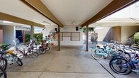 The outside entry and pool area at 801 D St in Davis, California offers a well-organized and functional communal exterior space designed to serve residents with everyday conveniences. The entry area features a covered, open-air structure with a concrete floor that provides shelter for bicycle parking, with multiple bike racks accommodating a generous number of bicycles — reflecting the bike-friendly culture of Davis. A centrally located mailbox station is positioned within this covered zone, offering easy access for residents. Decorative touches, including colorful hanging ornaments near the bike area, add a welcoming, community-oriented character to the space. Beyond the covered entry, the grounds open up to neatly manicured landscaping, featuring trimmed hedges, lush green lawns, and mature shade trees that create a pleasant, park-like atmosphere. Concrete walkways wind through the greenery, connecting the entry to the parking area and other parts of the property. A gated entry provides a layer of security while maintaining an open, accessible feel. The overall ambiance of the exterior is clean, well-maintained, and thoughtfully landscaped, offering residents an inviting arrival experience in a community-focused setting.