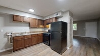 This single-floor unit offers a practical and well-organized layout with consistent design elements carried throughout each room. The kitchen serves as a functional centerpiece, featuring rich medium-toned wood cabinetry with ample upper and lower storage, granite-style countertops, a double sink, and a full suite of black appliances including a gas range and a full-size refrigerator. Light wood-style flooring runs through the kitchen, complementing the neutral gray wall tones found across the unit.

The living area is generously proportioned, featuring dark hardwood-style flooring, neutral gray walls, white baseboards, and windows that draw in natural light with views of surrounding greenery. A textured ceiling adds a subtle architectural detail to the space.

The bedrooms are well-sized and finished with light wood-style flooring and the same soft gray palette. One bedroom features two side-by-side closets, providing notable storage capacity, while another offers a large picture window framing tree-lined outdoor views.

The bathroom includes a tiled tub-shower combination with beige square tile surround, a window above the tub for natural light and ventilation, and wood-style flooring. The overall ambiance of the unit is clean, neutral, and move-in ready.