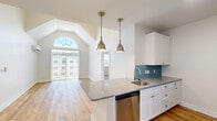Located in Mystic, CT, this well-designed 2-bedroom, 2-bathroom residence offers a thoughtful layout across a single floor. The open-concept living and kitchen area is an immediate standout, highlighted by soaring vaulted ceilings and a striking arched window that floods the space with natural light. A sliding glass door with vertical blinds provides access to outdoor views and enhances the airy ambiance throughout.

The kitchen is appointed with crisp white cabinetry, granite countertops, a teal subway tile backsplash, stainless steel appliances including a dishwasher and refrigerator, and a peninsula with an undermount sink. Pendant lighting with brushed gold fixtures adds a warm, refined touch to the space.

Both bedrooms feature warm-toned hardwood flooring and natural light from well-positioned windows. The spacious primary bedroom includes a wall-mounted split HVAC unit for personalized climate control. The two bathrooms are finished consistently with granite vanity tops, white cabinetry, and hardwood floors. One bathroom features a glass-enclosed walk-in shower with classic white subway tile, while the second offers a clean, functional layout with a full vanity.

Consistent hardwood flooring runs throughout the entire residence, unifying the space with a clean, modern aesthetic that complements the bright, neutral color palette.