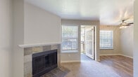 This single-floor residence offers a thoughtfully laid-out living environment with a blend of comfort and functionality. The living room serves as the heart of the home, anchored by a striking stone-tile surround fireplace with a classic mantle. Neutral-toned carpet flows throughout the space, complementing the soft, warm wall colors. Large windows fitted with white horizontal blinds invite an abundance of natural light, while a sliding glass door provides direct access to a private outdoor balcony, offering views of surrounding greenery.

The kitchen is well-appointed with rich dark wood cabinetry, light countertops, white subway tile backsplash, and a full suite of stainless steel appliances including a range, microwave, refrigerator, and dishwasher. Wood-look flooring runs the length of the kitchen, adding warmth and practicality to the space.

The bedrooms are carpeted and finished with clean, neutral walls, creating calm and versatile rooms. Each bedroom benefits from generous closet storage, including one with a set of wide sliding doors revealing a built-in shelving unit and hanging rod. Paneled interior doors throughout the home lend a cohesive, polished aesthetic. Overall, the space presents a clean, move-in-ready environment with practical features and a welcoming ambiance.