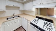 Located at 175 S Rio Vista St in Anaheim, California, this single-floor unit offers a practical and comfortable layout designed for everyday living. The living area is a standout feature, showcasing dark hardwood-style flooring, warm neutral-toned walls, and a textured ceiling. A ceiling fan provides airflow, while a wall-mounted air conditioning unit ensures year-round comfort. Sliding glass doors flood the space with natural light and open to a private outdoor patio area, extending the living space outdoors. The open layout flows naturally toward the kitchen, which features white cabinetry with brushed nickel hardware, light-toned countertops, a double stainless steel sink, a gas range, and a dishwasher — offering ample storage and functionality for cooking and meal prep. The bedroom is finished with plush carpeting and neutral walls, creating a calm and restful environment. A closet with a hanging rod provides dedicated storage. The bathroom is well-equipped with an extended vanity topped with light countertops, white cabinetry, a large mirror with overhead lighting, dark hardwood-style flooring, and a full bathtub and shower combination. Clean white trim and consistent finishes throughout the unit tie the overall design together cohesively.