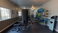 Located at 7000 S Paradise Rd in Las Vegas, Nevada, this fitness center offers a comprehensive workout facility across a single floor. The space is divided into two functional zones designed to support a full range of exercise routines. The strength and functional training area is lined with floor-to-ceiling mirrors that enhance the sense of space, and features a multi-use cable resistance machine with an adjustable bench, a squat rack, resistance bands, stability balls in multiple sizes, exercise mats, and additional free weight accessories — all organized for easy access. The flooring throughout is a durable rubber material, ideal for high-impact activities. The cardio zone is bright and welcoming, with natural light streaming in through a large window. It houses an elliptical trainer, a recumbent bike, and an upright stationary bike, providing a variety of low-impact cardiovascular options. A ceiling fan keeps air circulating comfortably throughout the room. Informational notices are posted on the walls, and the overall layout is clean and practical. Together, both areas create a well-rounded fitness environment suited for strength training, cardio exercise, flexibility work, and functional fitness.
