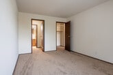 This single-floor residential unit offers a practical and straightforward layout designed for comfortable everyday living. The main living area is finished with neutral-toned carpet and features a ceiling fan, providing a simple and functional space. A wood-paneled entry door adds a classic touch to the entryway.

The kitchen is equipped with cream-colored cabinetry, dark laminate countertops, a double stainless steel sink, a dishwasher, and a full-size refrigerator, all set atop durable tile flooring that contrasts with the carpeted areas throughout the rest of the unit.

The bedrooms are well-proportioned, each featuring plush carpet, vertical blinds over windows that invite natural light, and baseboard heating units along the walls. One bedroom includes an expansive open closet system with built-in shelving and multiple hanging rods, offering ample storage.

The unit includes two bathrooms. The full bathroom features a tub and shower combination with classic yellow tile surround, mosaic tile flooring, and a toilet. The second bathroom offers a vanity with a wood-framed mirror, a single-basin sink, chrome fixtures, and accessory bars. Both bathrooms maintain a clean, functional aesthetic suited for daily use.