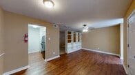 This single-floor residence offers a cohesive and functional layout with warm, inviting interiors throughout. The main living area is anchored by rich, dark hardwood flooring that extends seamlessly across the space, complemented by neutral tan walls and white baseboards that create a clean, balanced aesthetic. A ceiling fan with a light fixture provides both comfort and illumination, while multiple windows fitted with blinds allow for adjustable natural light. A distinctive white open-shelving unit serves as a partial room divider, offering both storage and a subtle separation between the living and adjoining areas.

The kitchen is efficiently designed with white cabinetry, granite-style countertops, a stainless steel double sink, a tile backsplash in warm earth tones, and black appliances including a dishwasher and refrigerator. The textured ceiling adds architectural character throughout the space.

The bathroom area features a vanity with a granite-style countertop, an undermount sink, and a mirrored cabinet above. Adjacent to the vanity is a generously sized walk-in closet outfitted with multiple shelving tiers and carpeted flooring, providing ample organized storage. The front entry opens into the living area, flanked by windows that fill the space with natural light, creating a welcoming and open atmosphere from the moment you arrive.