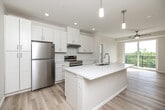Located at 545 Market St in West Des Moines, Iowa, this well-designed one-bedroom, one-bathroom unit offers a thoughtful layout that maximizes comfort and functionality. The open-concept living and kitchen area is anchored by a large central island with a white quartz countertop and integrated sink, complemented by crisp white shaker cabinetry, stainless steel appliances including a refrigerator and electric range, and elegant pendant lighting. Light hardwood flooring flows throughout the main living space, enhancing the bright, airy atmosphere. The living area extends seamlessly toward a sliding glass door that opens onto a private balcony with outdoor views of the surrounding greenery, and a ceiling fan overhead adds both style and practicality. The bedroom features soft wall-to-wall carpeting, a large window that fills the room with natural light and tree-lined views, and access to a dedicated closet. The bathroom is finished with large-format marble-look tile flooring, a single vanity with understated cabinetry, and an accessible shower equipped with grab bars. Clean neutral tones, modern hardware, and consistent finishes throughout give this unit a cohesive, contemporary feel well-suited for comfortable everyday living.