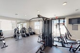 Located at 12730 W Camelback Rd in Litchfield Park, Arizona, this single-level fitness center offers a well-organized and comprehensively equipped workout facility. The space features durable rubber flooring throughout, providing a safe and functional surface for a wide range of exercise activities. Recessed lighting in the white ceiling keeps the room bright and well-illuminated, while multiple windows fitted with blinds allow ample natural light to filter in and offer views of the surrounding area.

The cardio zone is equipped with treadmills, elliptical trainers, and a rowing machine, complemented by a wall-mounted flat-screen television for entertainment during workouts. A large Body-Solid Pro Club multi-station cable machine serves as the centerpiece for strength training, supported by an adjustable workout bench and a full rack of dumbbells alongside a colorful medicine ball rack. Full-length mirrors along one wall enhance the sense of space and allow users to monitor their form.

Near the entrance, a wall-mounted water fountain provides convenient hydration, and motivational fitness posters add an energetic atmosphere to the space. Multiple access doors and clearly marked emergency exits ensure safe and easy entry and exit throughout the facility.
