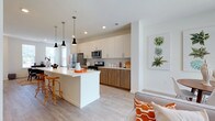 This contemporary two-story residence offers a thoughtfully designed layout with clean lines and modern finishes throughout. The open-concept main floor centers around a sleek kitchen equipped with stainless steel appliances, two-tone cabinetry featuring white uppers and warm wood-grain lowers, a subway tile backsplash, and a generous island with a white quartz countertop and pendant lighting overhead — ideal for casual dining or entertaining. Light wood-tone flooring flows seamlessly into the adjacent living area, which is bright and airy thanks to large windows and sliding glass doors. A dedicated dining area sits nearby, bathed in natural light from multiple windows and accented by neutral walls that complement the space's modern aesthetic. A full bathroom with wood-grain vanity cabinetry is conveniently located on the main level. Upstairs, the bedrooms offer plush carpeting and ample natural light through well-proportioned windows. The primary bedroom is spacious and connects to an en-suite bathroom featuring a double-sink vanity, a glass-enclosed walk-in shower, and wood-finish cabinetry. An additional full bathroom with a single vanity and shower serves the remaining bedrooms. Throughout, the design maintains a cohesive, contemporary palette of whites and warm wood tones, creating a bright and welcoming atmosphere.