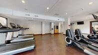Located at 11260 Point East Dr in Rancho Cordova, CA, this dedicated fitness center offers a well-appointed exercise space designed to support a full workout experience. The room is thoughtfully laid out across a single floor, providing ample open space for movement and equipment use.

The cardio zone features multiple Life Fitness treadmills and elliptical machines positioned along the perimeter, complemented by a multi-function cable strength training machine situated on durable rubberized flooring. The remainder of the room is finished with rich, hardwood-style flooring that adds warmth to the clean, modern aesthetic.

Large wall-mounted mirrors enhance the sense of space and provide visual feedback during exercise, while wall-mounted flat-screen televisions offer entertainment options throughout a workout. Recessed lighting in the tray ceiling provides bright, even illumination throughout the space.

Natural light pours in through sliding glass doors that open to an outdoor terrace or pool area, creating a refreshing, airy atmosphere. Neutral-toned walls with a subtle textured wallcovering contribute to a polished, professional environment. A small storage and service alcove with a wooden shelving unit is tucked toward the rear of the room. The space is climate-controlled and equipped with a wall-mounted thermostat for personalized comfort.