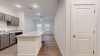 This single-floor, one-bedroom, one-bathroom unit offers a thoughtfully designed layout that maximizes its compact footprint. The open-concept living and kitchen area forms the heart of the space, anchored by a central peninsula island topped with granite-style countertops, which serves as both a prep surface and casual dining area. The kitchen is equipped with gray shaker-style cabinetry, matching granite countertops, and a full suite of black appliances including a refrigerator, range, microwave, and dishwasher. Recessed lighting and a ceiling fan illuminate the main living area, which benefits from natural light through multiple windows fitted with blinds. Wood-style plank flooring runs consistently throughout the unit, lending a cohesive, modern aesthetic. The bedroom is a well-proportioned room featuring a large window, a ceiling fan, and access to a dedicated walk-in closet outfitted with multi-level wire shelving systems for organized storage. The bathroom includes a granite-topped vanity with a wood-toned cabinet base, a framed mirror, and a tiled shower. Neutral white walls throughout create a clean, bright ambiance well-suited for personalization.