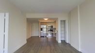 This single-floor space offers a clean, contemporary design centered around an open-concept living and kitchen area. Rich, dark hardwood flooring extends throughout, providing a warm contrast to the bright white walls and ceilings that keep the interior feeling airy and well-lit.

The kitchen is a standout feature, showcasing flat-panel cabinetry in a warm wood finish, a full suite of stainless steel appliances including a French door refrigerator with ice maker, a built-in microwave, and a gas range. A sleek peninsula with bar-height seating serves as both a functional workspace and a casual dining spot, creating a natural transition into the open living area.

A dedicated built-in shelving nook is tucked conveniently to the side, offering excellent storage and display opportunities without intruding on the main living space. The entry area is well-defined, with a solid door providing a clear threshold between the interior and the outside. Recessed and flush-mount ceiling lighting illuminates the space evenly throughout.

Overall, the layout is thoughtfully organized, balancing openness with functionality. The neutral color palette and modern finishes create a versatile backdrop well-suited to a variety of interior styles.